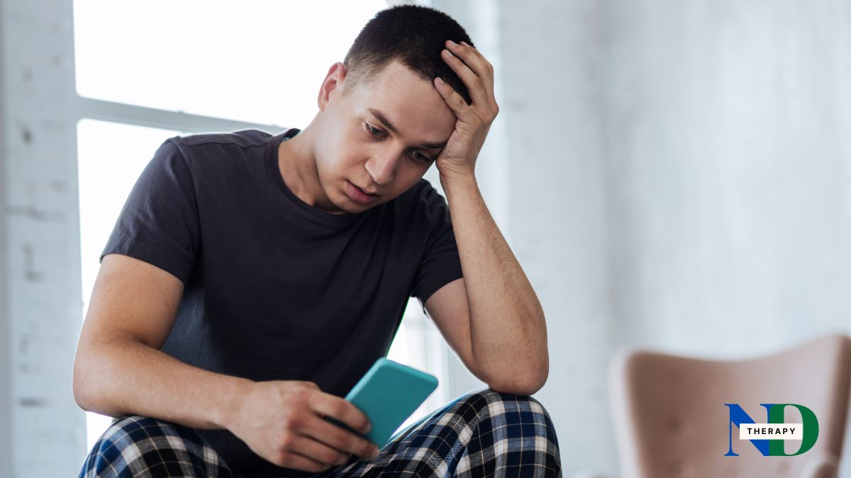 Man, sitting, looking at phone, frustrated.