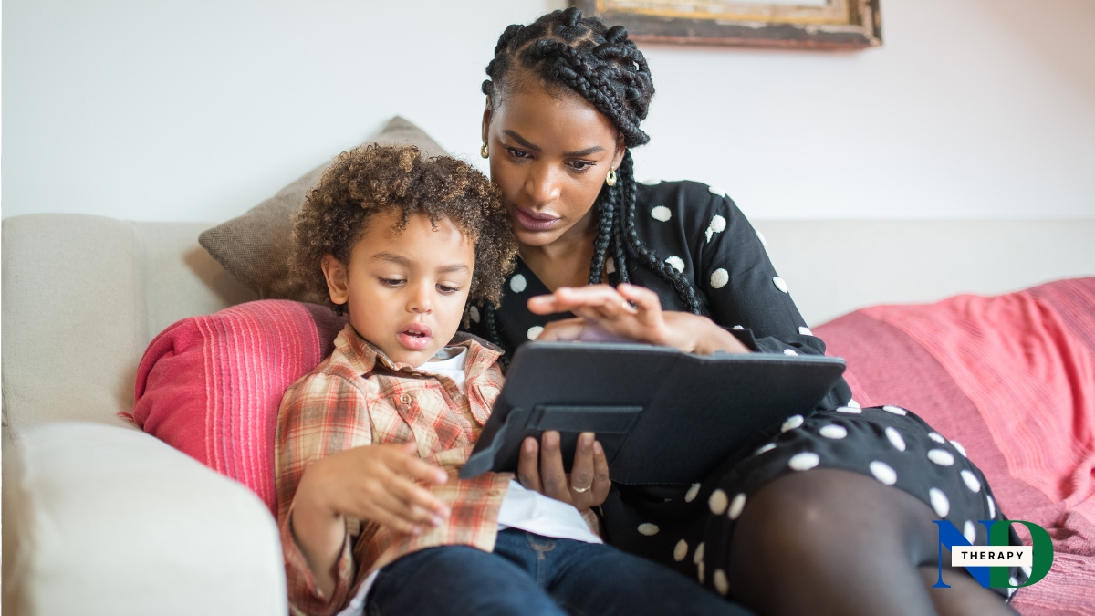 A mother and her autistic son looking at a tablet together on the couch, talking calmly.