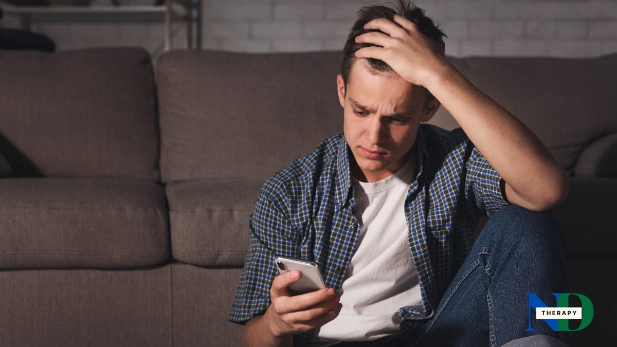 A teenager sitting alone in a bedroom looking at a phone, at the end of the day.